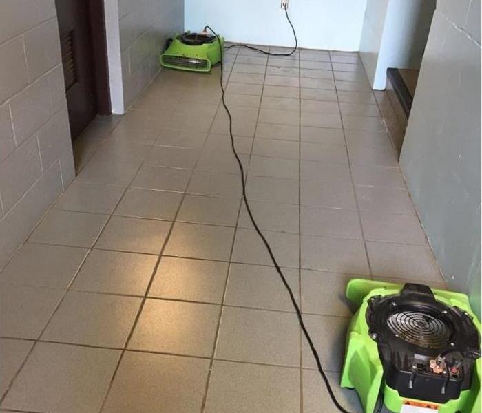 Tile floor in the hallway of a commercial building with two SERVPRO air movers set up during the dryout process.