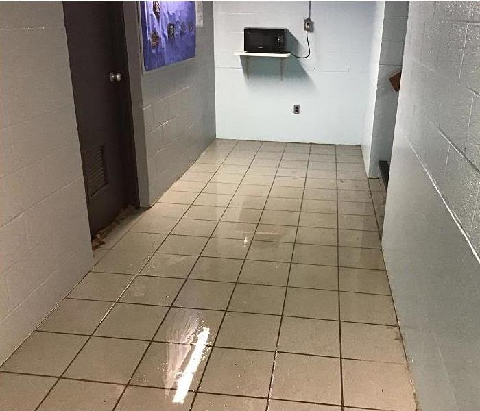 Hallway of a commercial building with standing water on the tile floor.