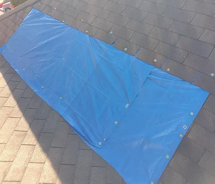 Roof of a home with a section covered by a blue tarp