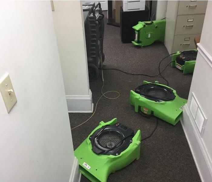 Room in an office with filing cabinets and four air movers and a dehumidifier set up in the room.