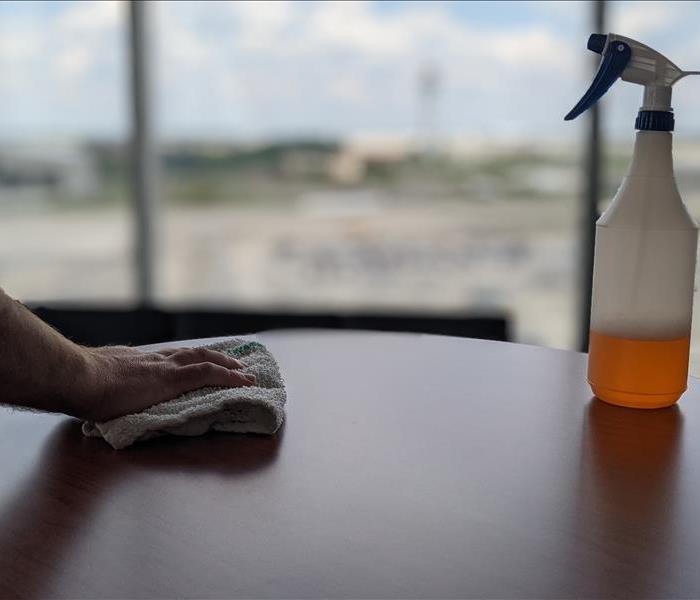 Hand on a towel wiping down a table next to a spray bottle.